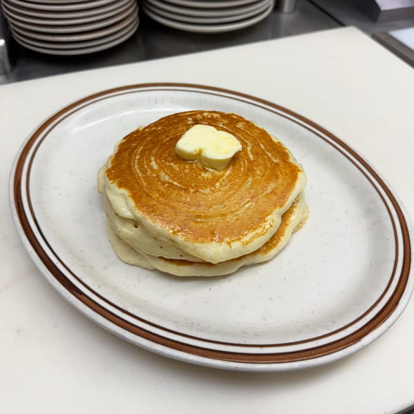 Stack of golden-brown pancakes with a melting pat of butter on a white plate with brown stripes.