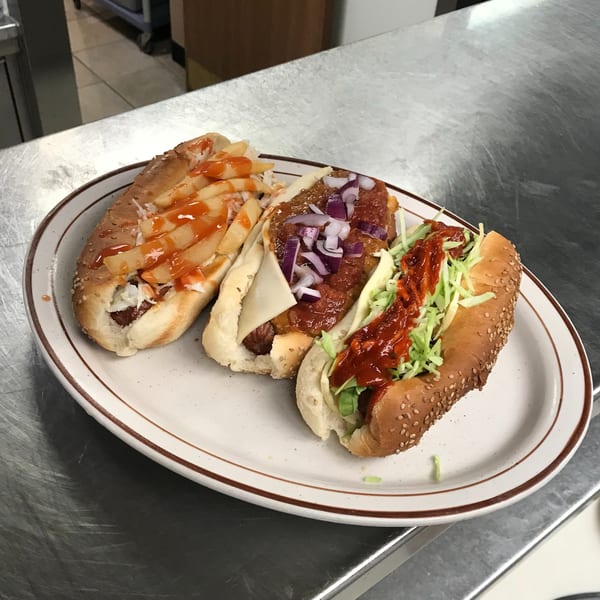 Three gourmet hot dogs with various toppings, including fries, chili, onions, and shredded lettuce.