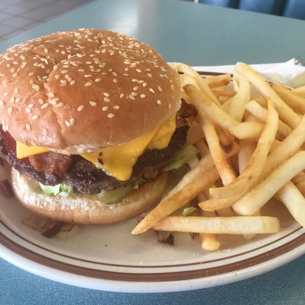 A bacon cheeseburger with lettuce and pickles, served with a side of golden french fries.