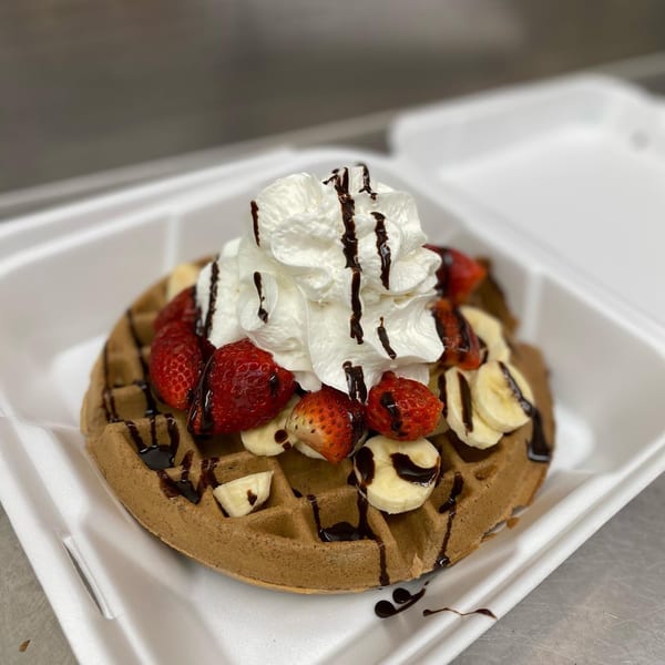 Zorbas Family Dining waffle with strawberries, bananas, whipped cream, and chocolate drizzle in a to-go container.