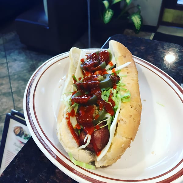 A hot dog with shredded lettuce, jalapeños, and red sauce on a white plate.