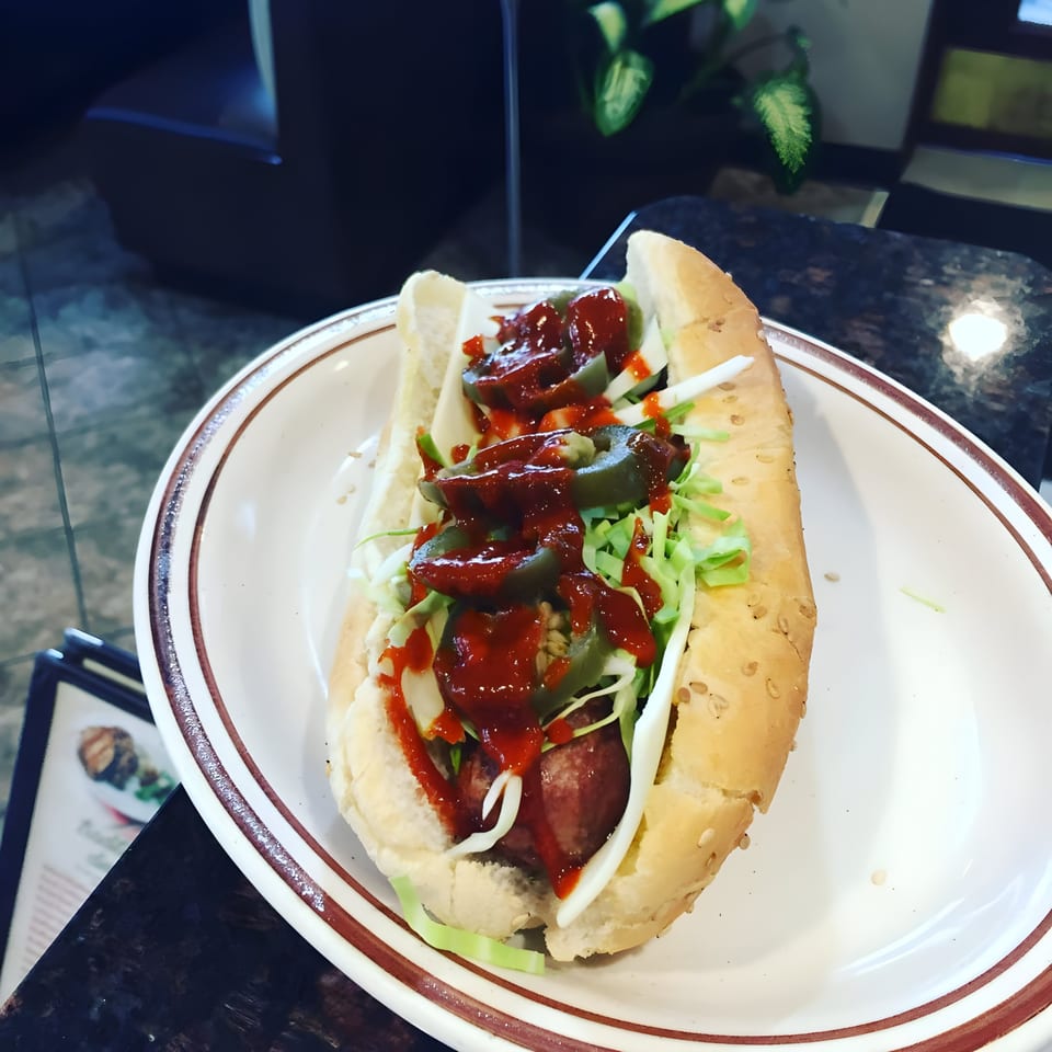 A hot dog with shredded lettuce, jalapeños, and red sauce on a white plate.
