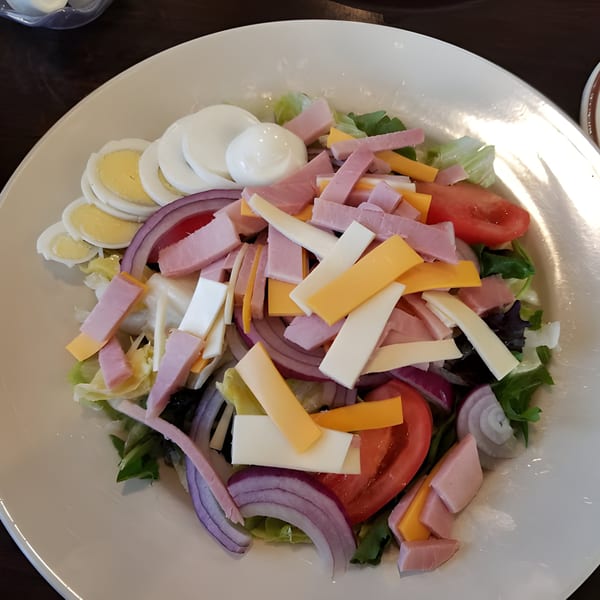 A chef salad with ham, cheese, hard-boiled eggs, tomatoes, and red onion on a bed of lettuce.