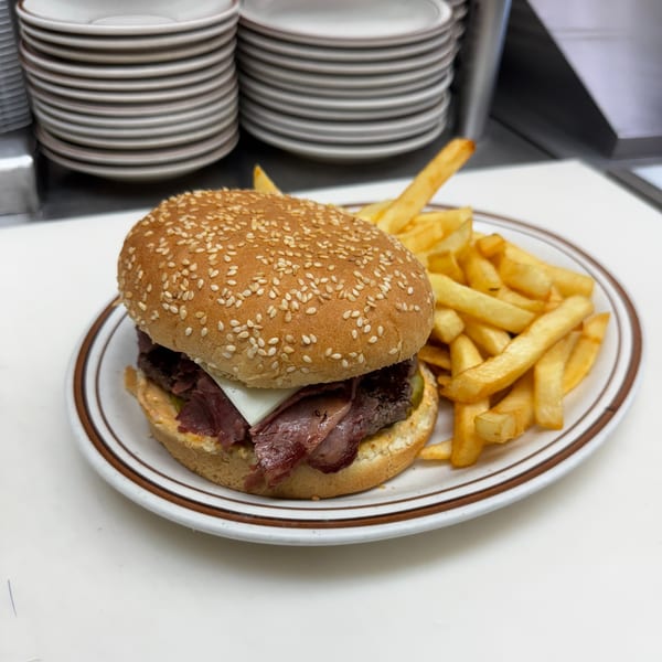 A roast beef sandwich with cheese on a sesame bun, served with a side of golden french fries.